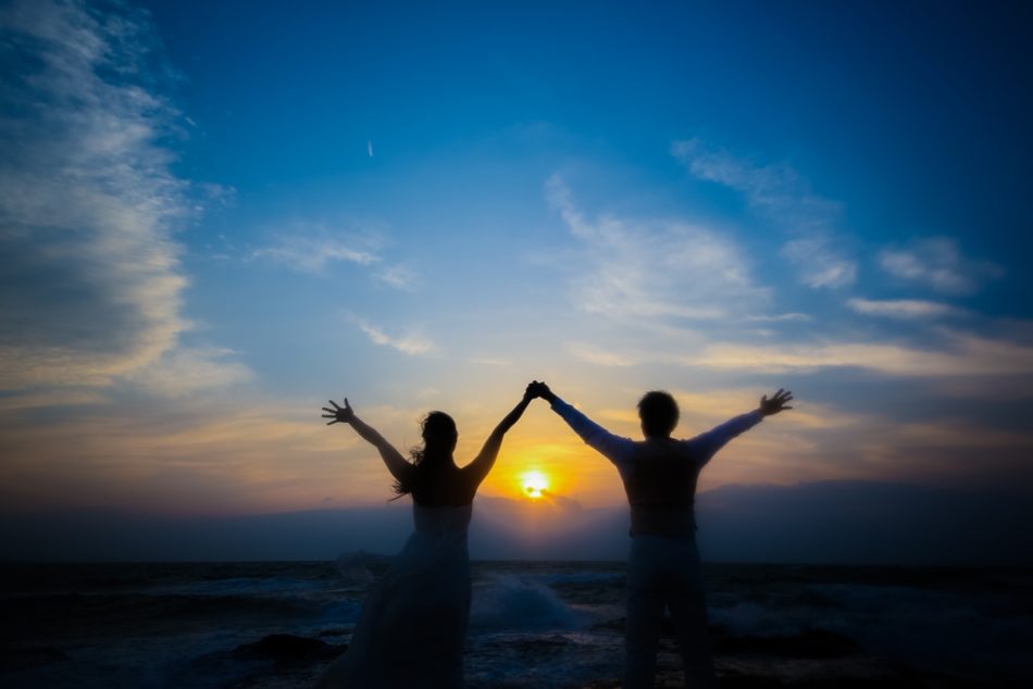 内海の夕日をバックに両手を挙げて撮った結婚写真