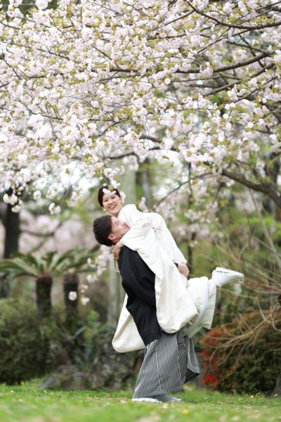 桜の木の下で新婦さんを抱き上げる新郎