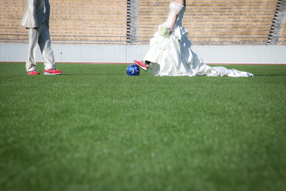 ウェディングドレスとタキシードを着てパロマ瑞穂サッカー場でサッカーしている夫婦