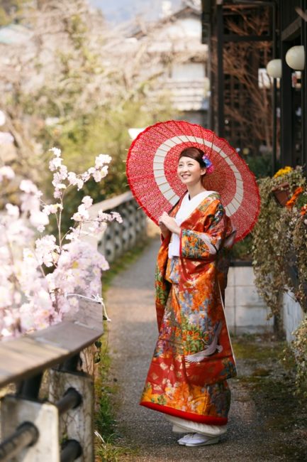 下町の桜と赤い和傘を持った笑顔の新婦様