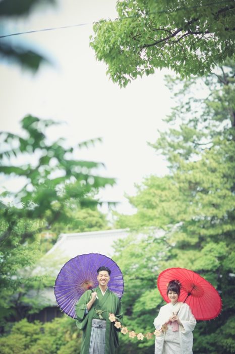 モスグリーンの紋付と白無垢姿で和傘をさしている夫婦