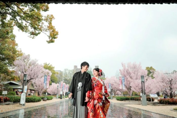 徳川園の桜のメイン通りに立つ和装を着た新郎新婦